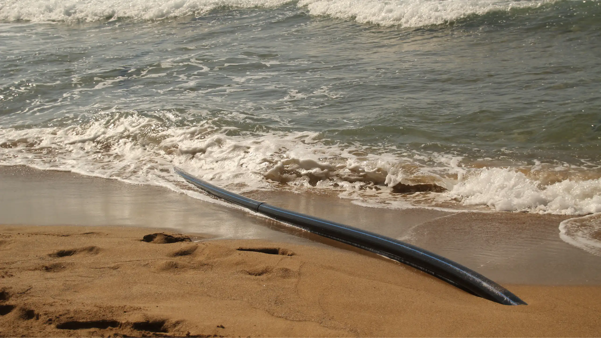 Gros plan sur le câble émergeant du sable et plongeant dans la mer.