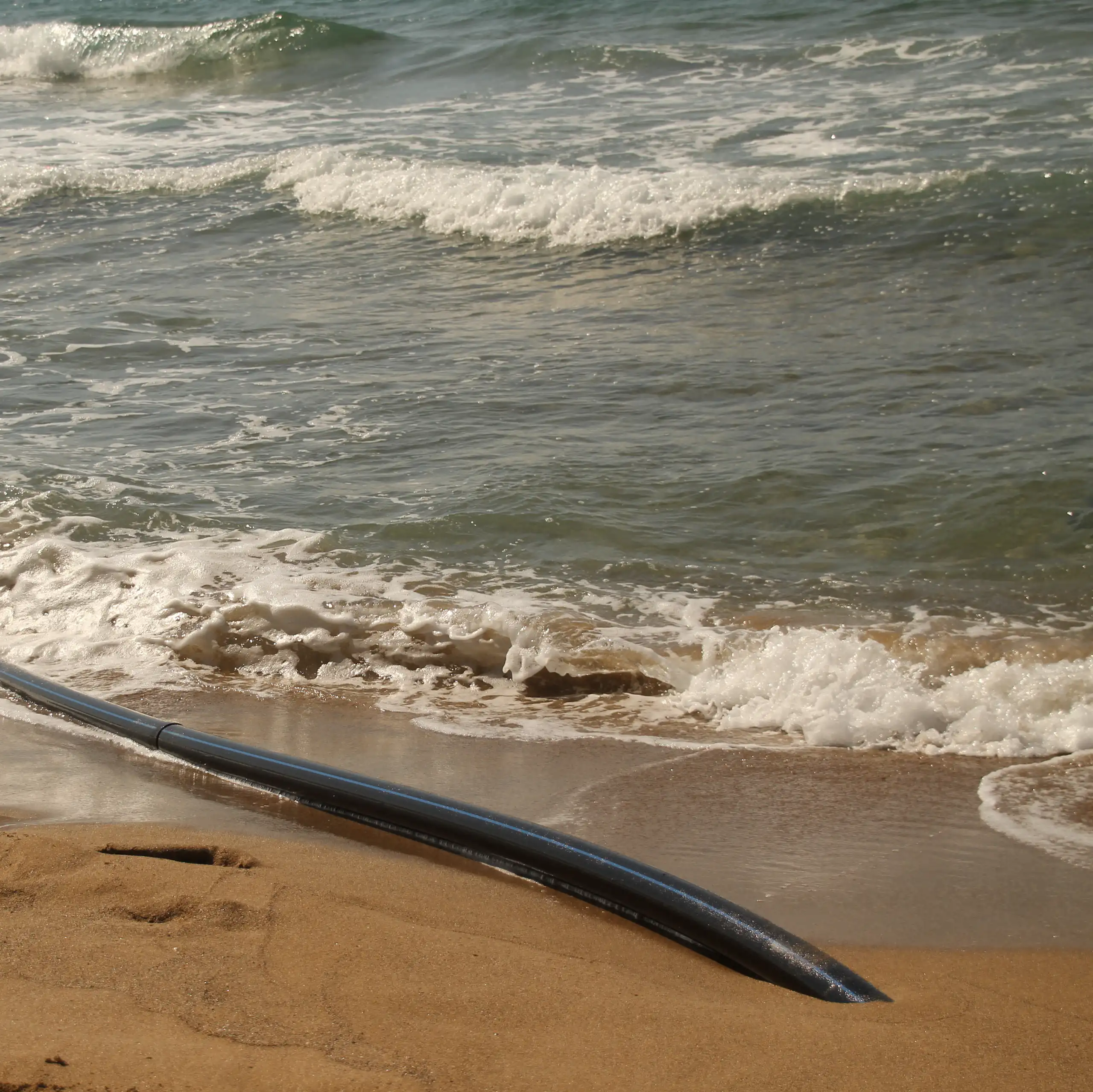 Gros plan sur le câble émergeant du sable et plongeant dans la mer.