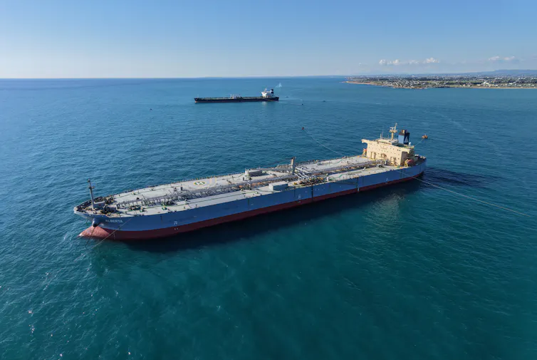 Large tanker ships float off a coastal area.