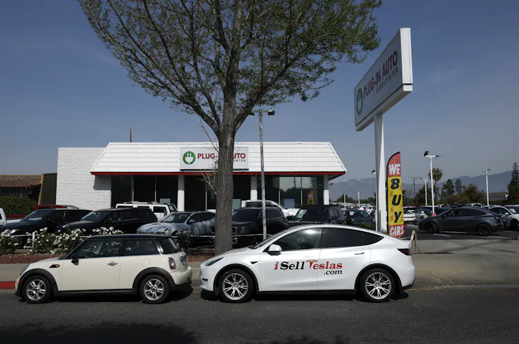 Electric cars sit on a street and in a parking lot.