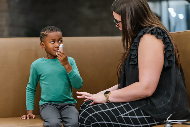 A young boy using an inhaler sits on a bench with an adult.