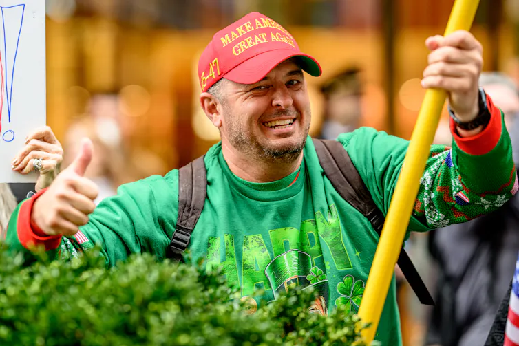 A man in a green sweater wears a red 'Make America Great Again' cap.