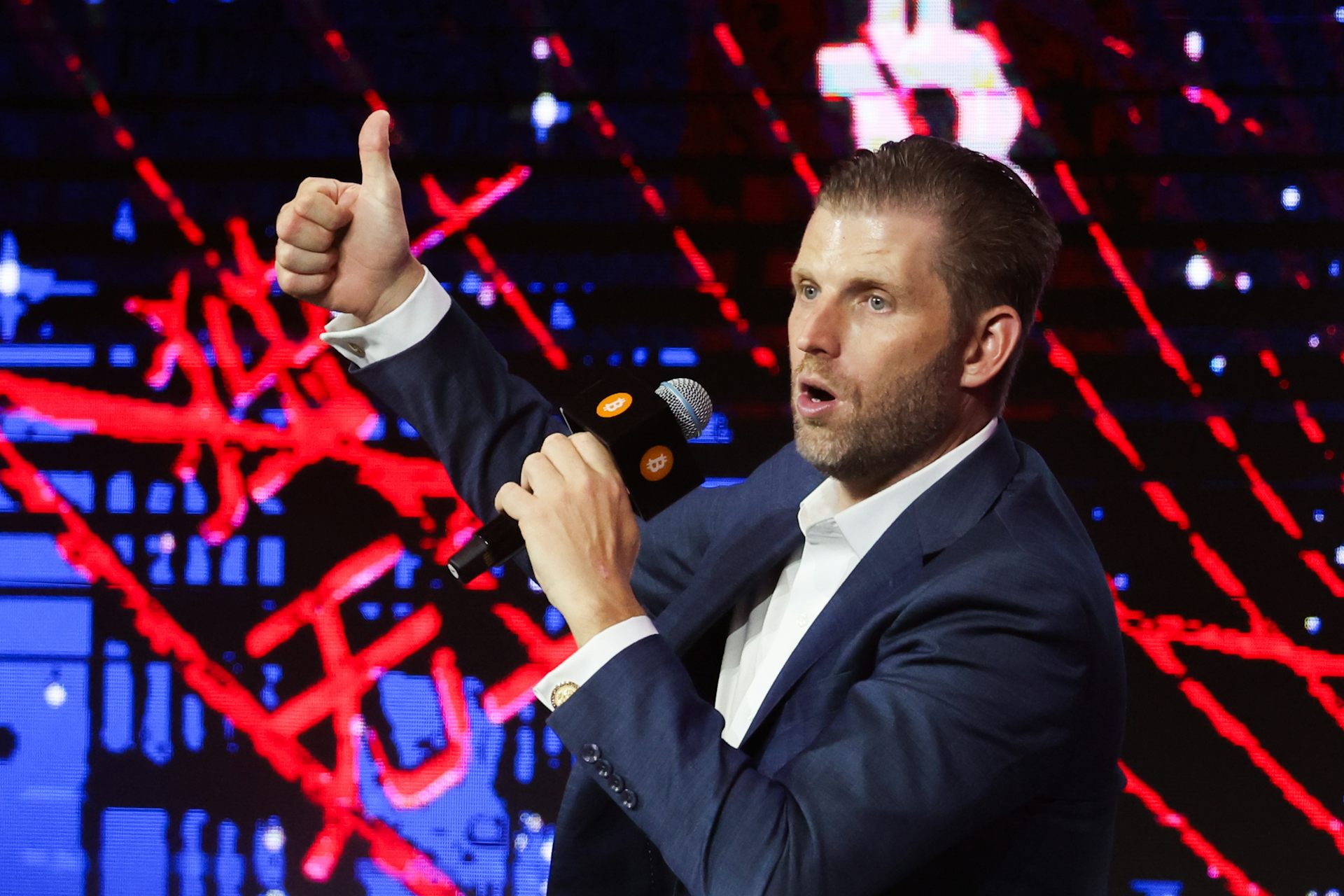 President Donald Trump's son Eric gestures to the crowd, standing against neon lights, as he speaks at the Bitcoin Asia 2025 conference in Hong Kong.