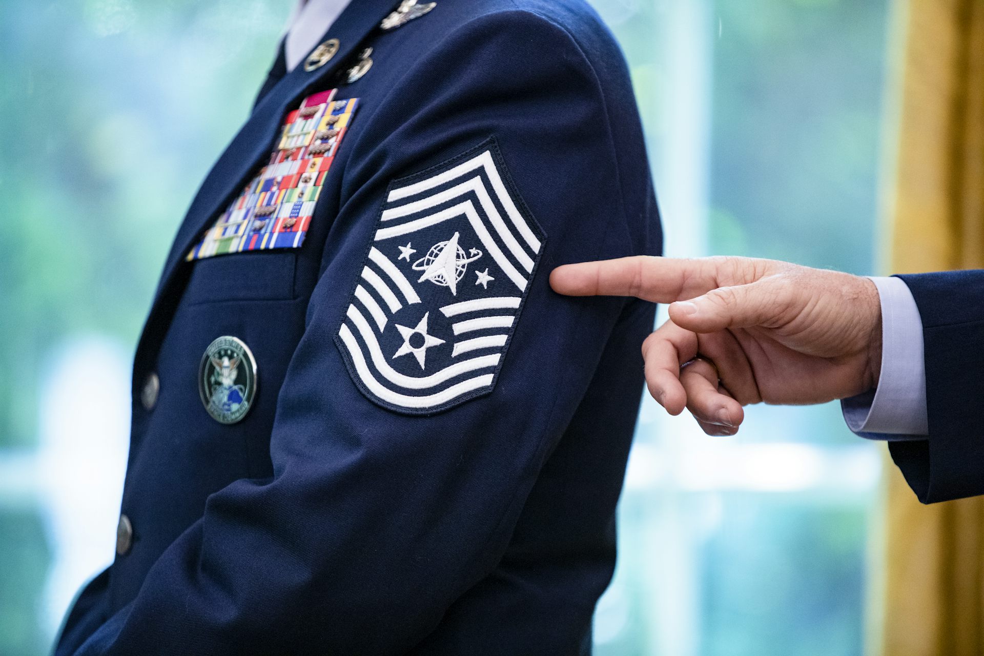 A hand points to a Space Force chevron rank insignia on the sleeve of a dark blue dress uniform