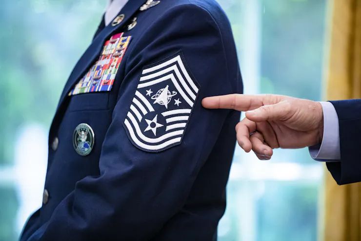 A hand points to a Space Force chevron rank insignia on the sleeve of a dark blue dress uniform