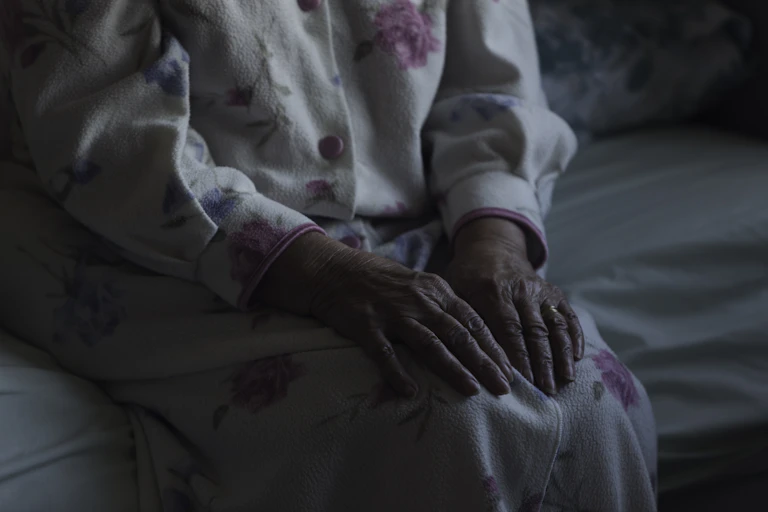 An old woman's hands on her lap in a dark room