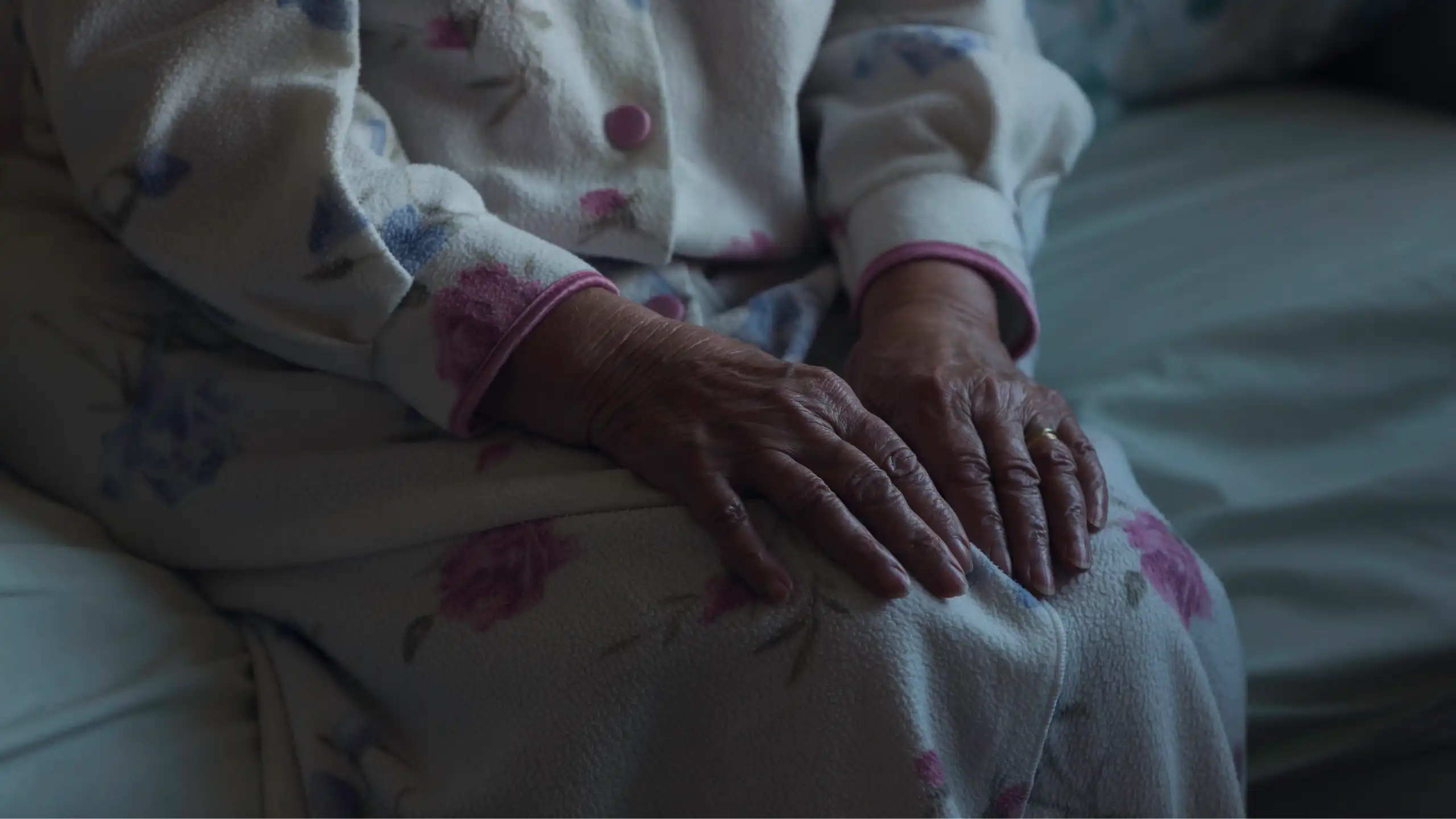 An old woman's hands on her lap in a dark room