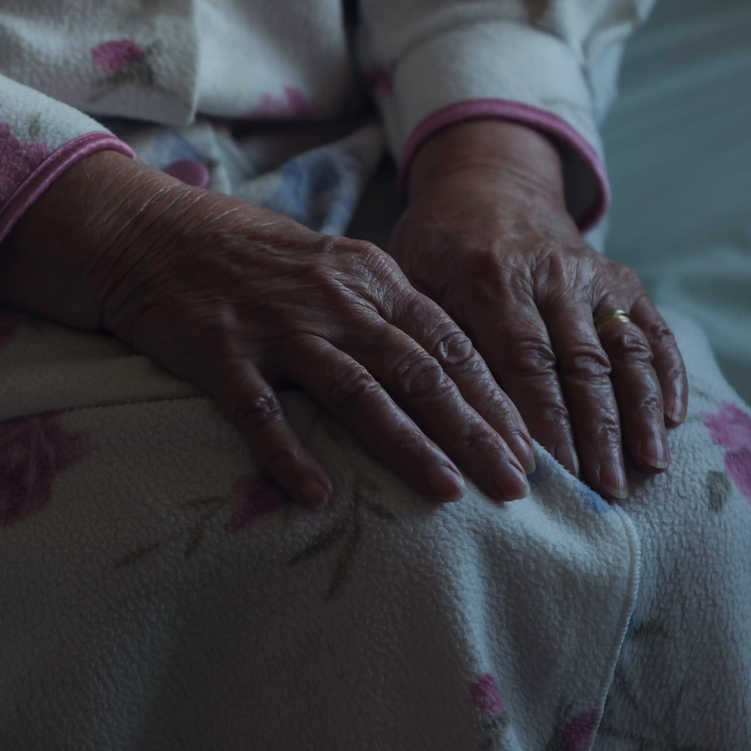 An old woman's hands on her lap in a dark room