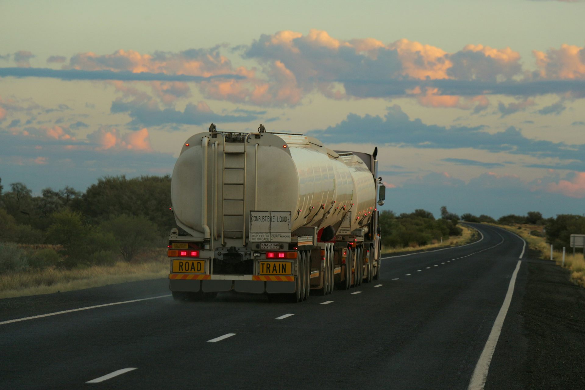 A large fuel tanker road train driving on a highway in the Australian outback.