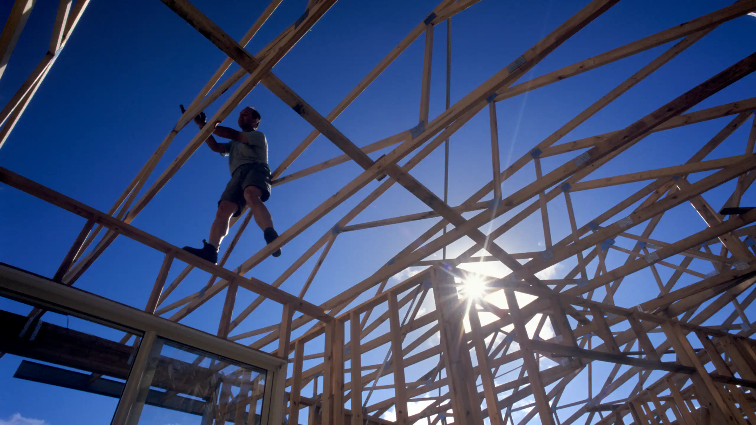 Silhouette of builder standing on timber house frame, low angle view.