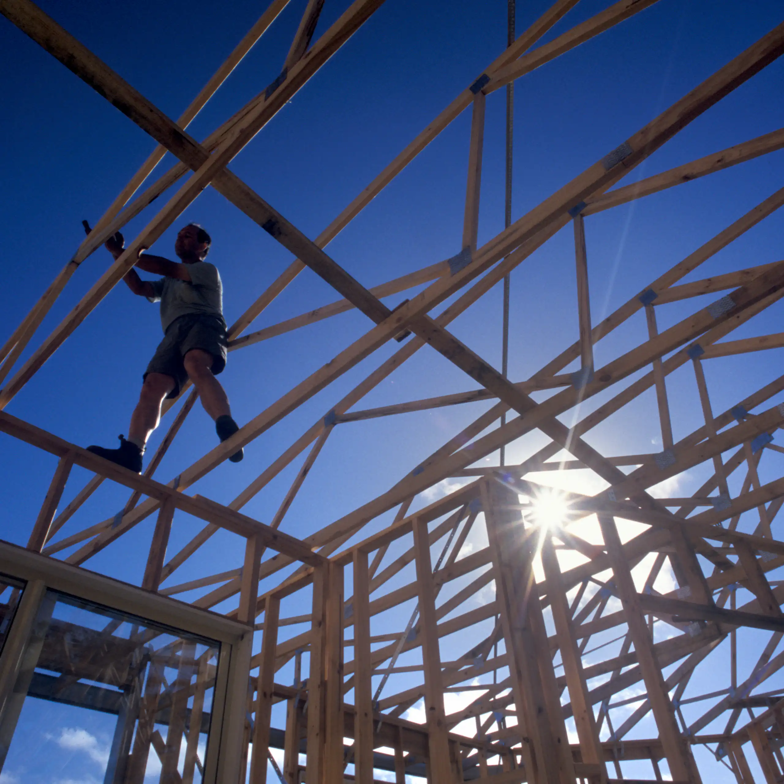 Silhouette of builder standing on timber house frame, low angle view.