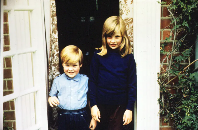 A small boy with his older sister, outside a house.
