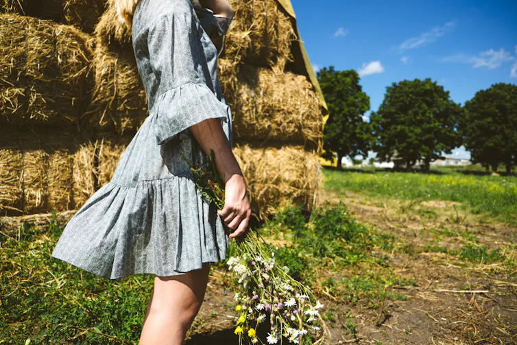 Woman with a bunch of flowers by hay bales.