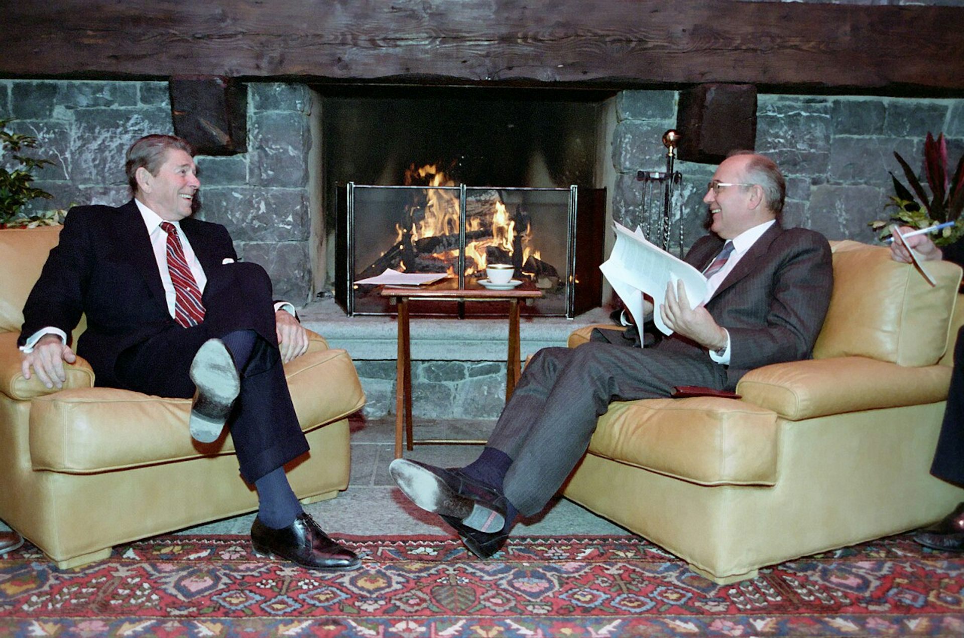 Ronald Reagan and Mikhail Gorbachev sit smiling at each other jn front of a log fire.