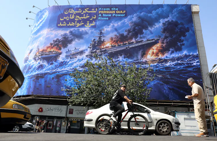 Iranians drive next to an anti-US billboard in Tehran, which reads in Persian: 'The devil army will drown in the Persian Gulf'.