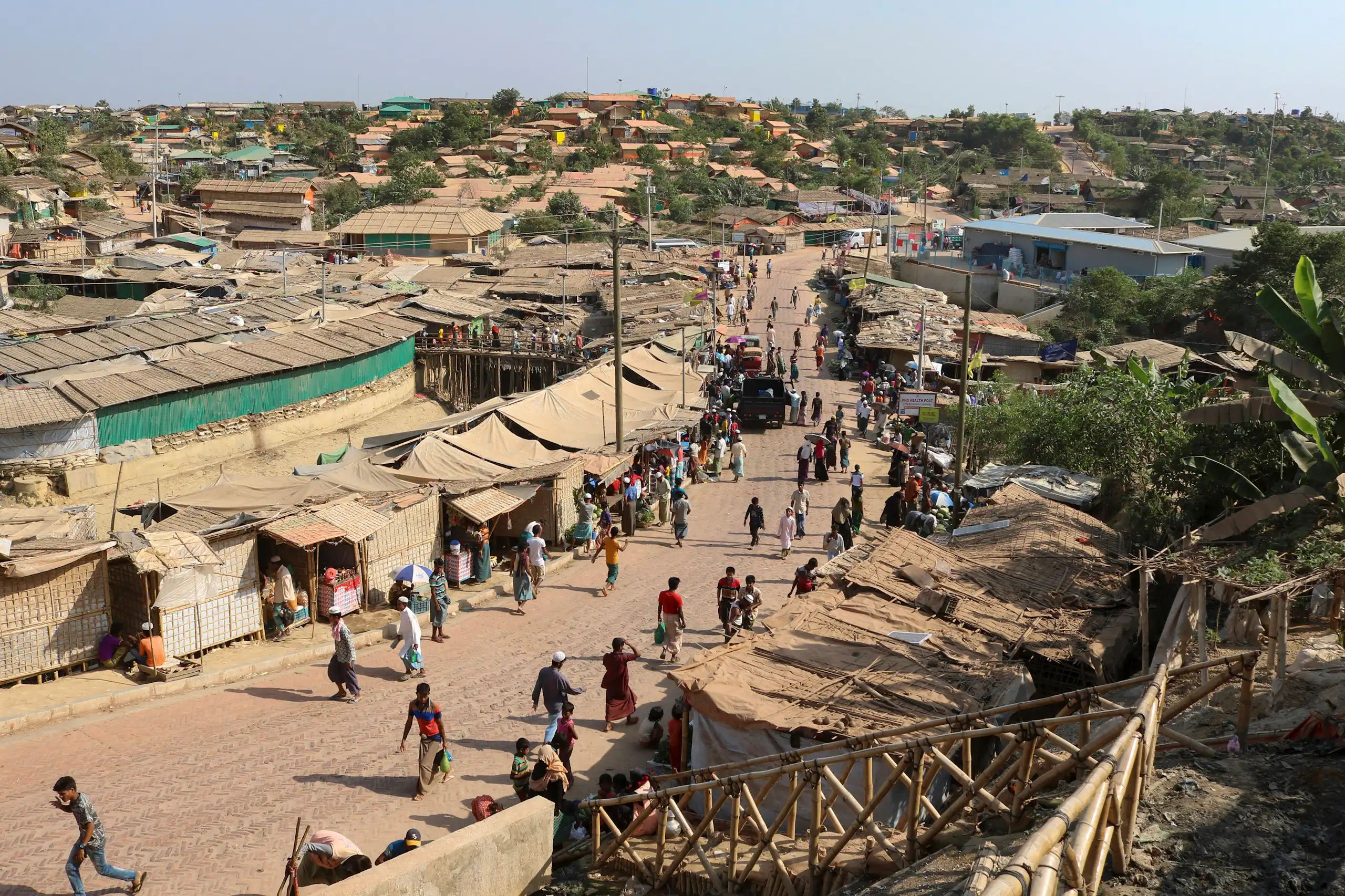 A long shot of a refugee camp where people are seen walking along a dusty road.