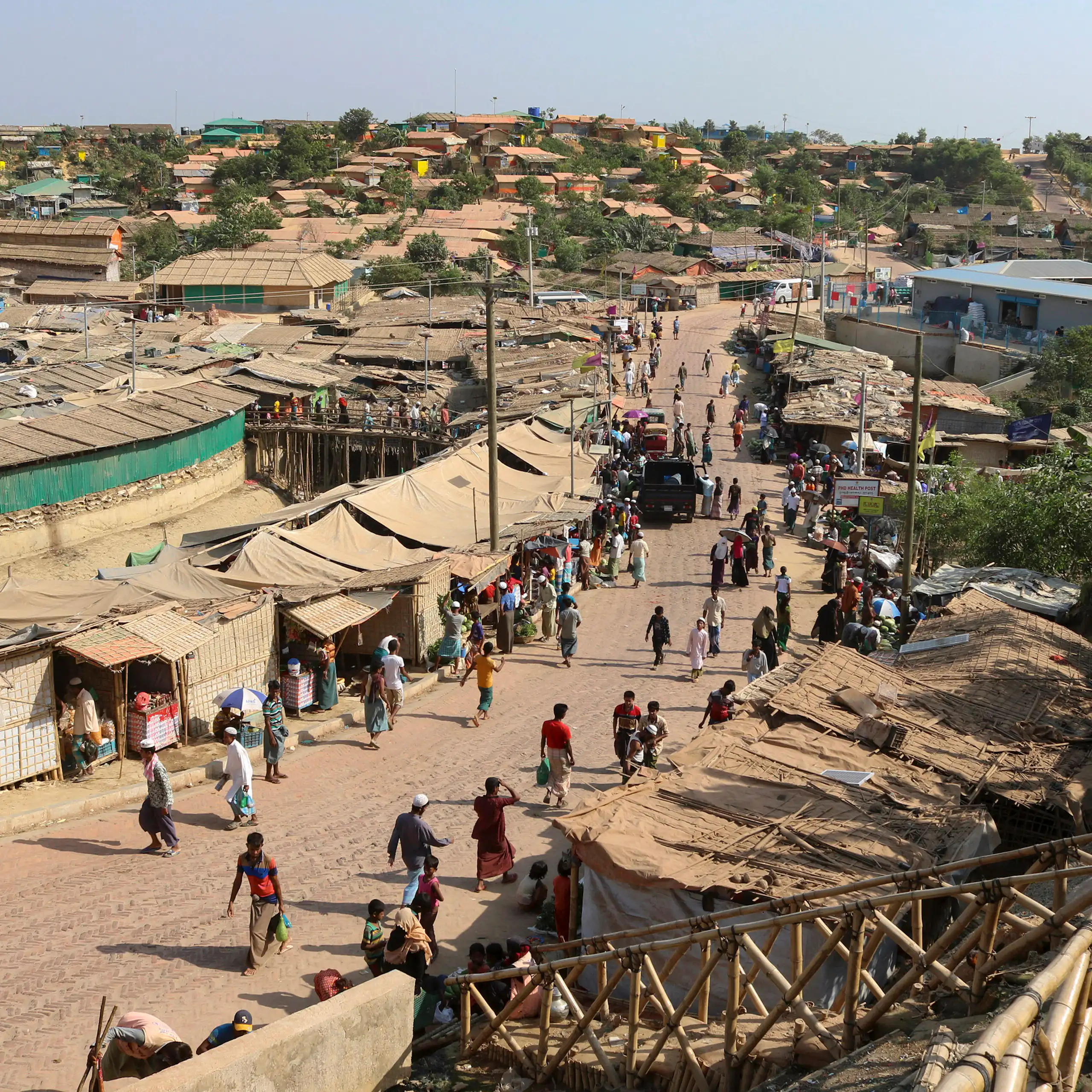 A long shot of a refugee camp where people are seen walking along a dusty road.