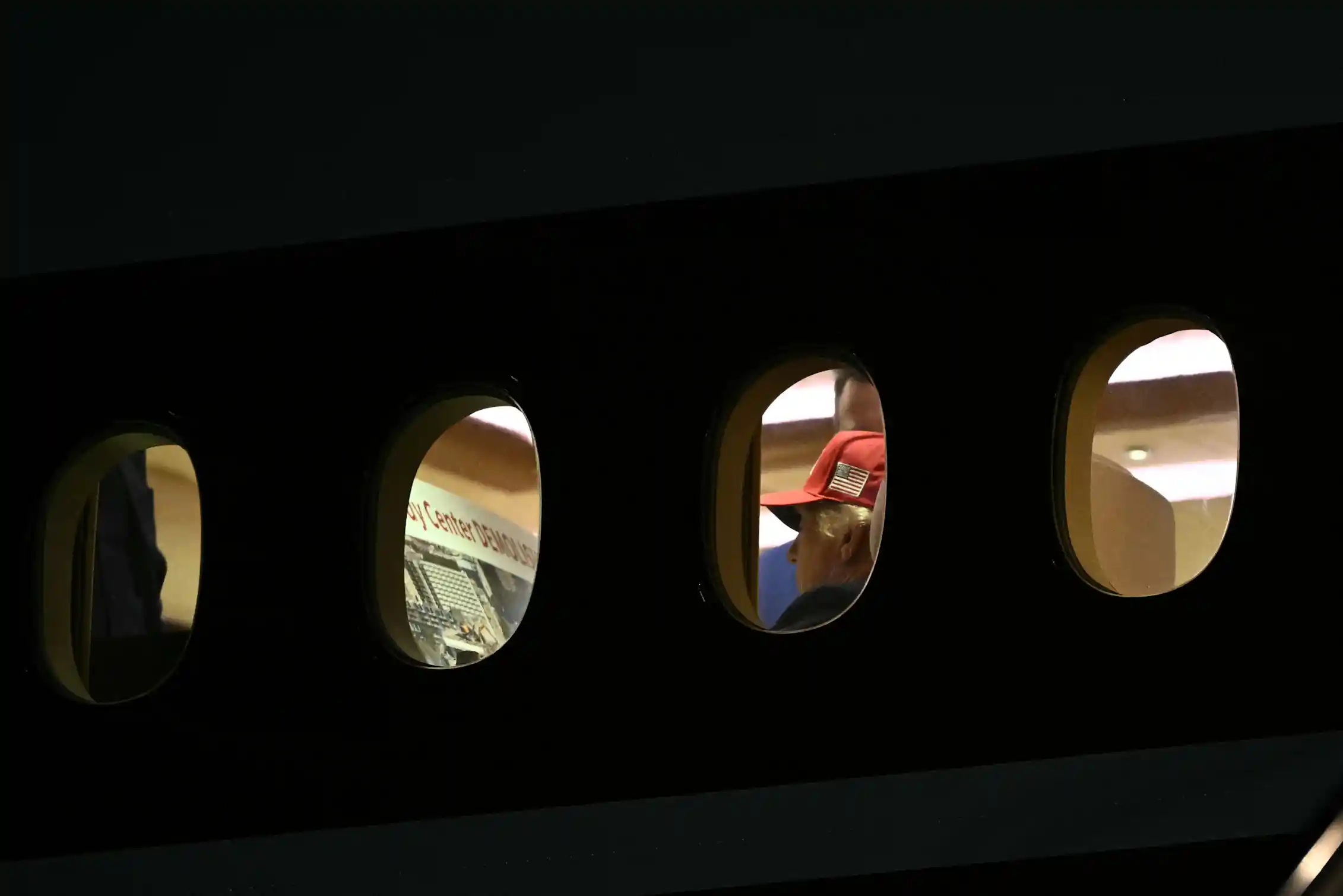 A man in a baseball cap is seen aboard an airplane, apparently reading the words
