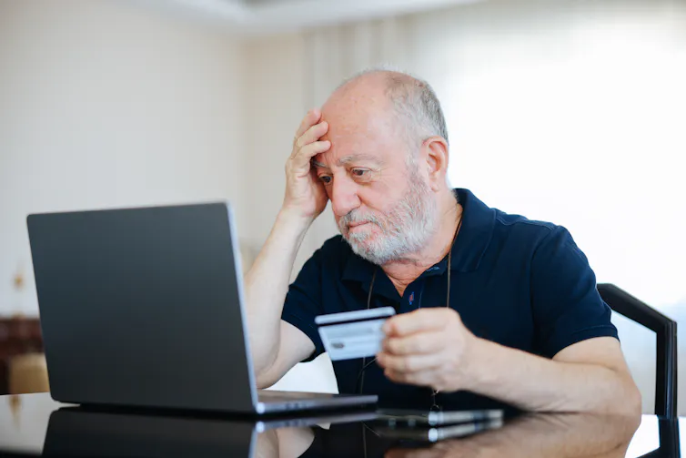 older man sitting in front of his computer with his credit card