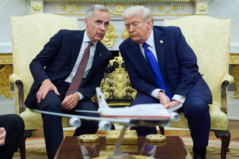two aged white men with greying hair sit in a gaudy room with gold finishes. they sit on gold coloured chairs leaning toward each other. a toy-like miniature of a passenger plane is on the table in front of them.