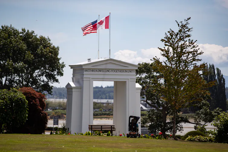 canadian and American flags on poles above a white arch in a park