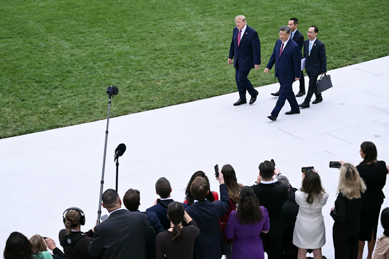 Two men walk down a white path next to a green lawn.