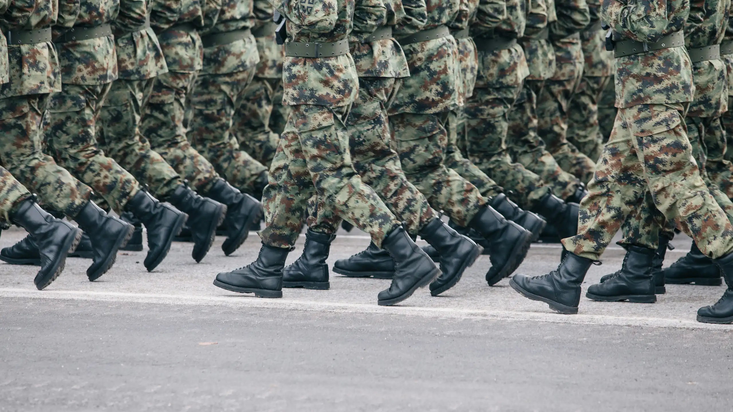 The legs of rows of soldiers in camouflage uniform and boots marching on a tarmac road
