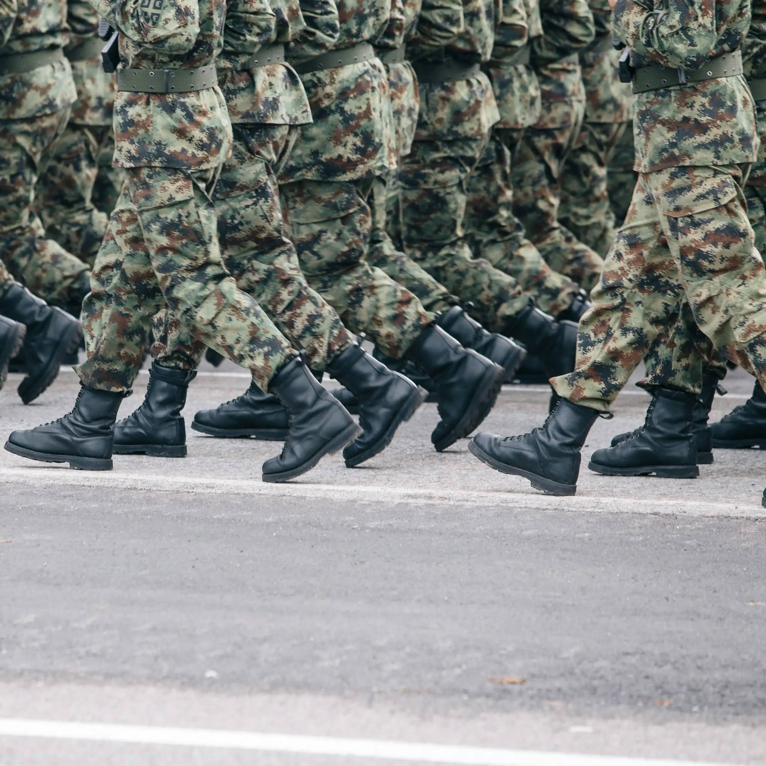 The legs of rows of soldiers in camouflage uniform and boots marching on a tarmac road