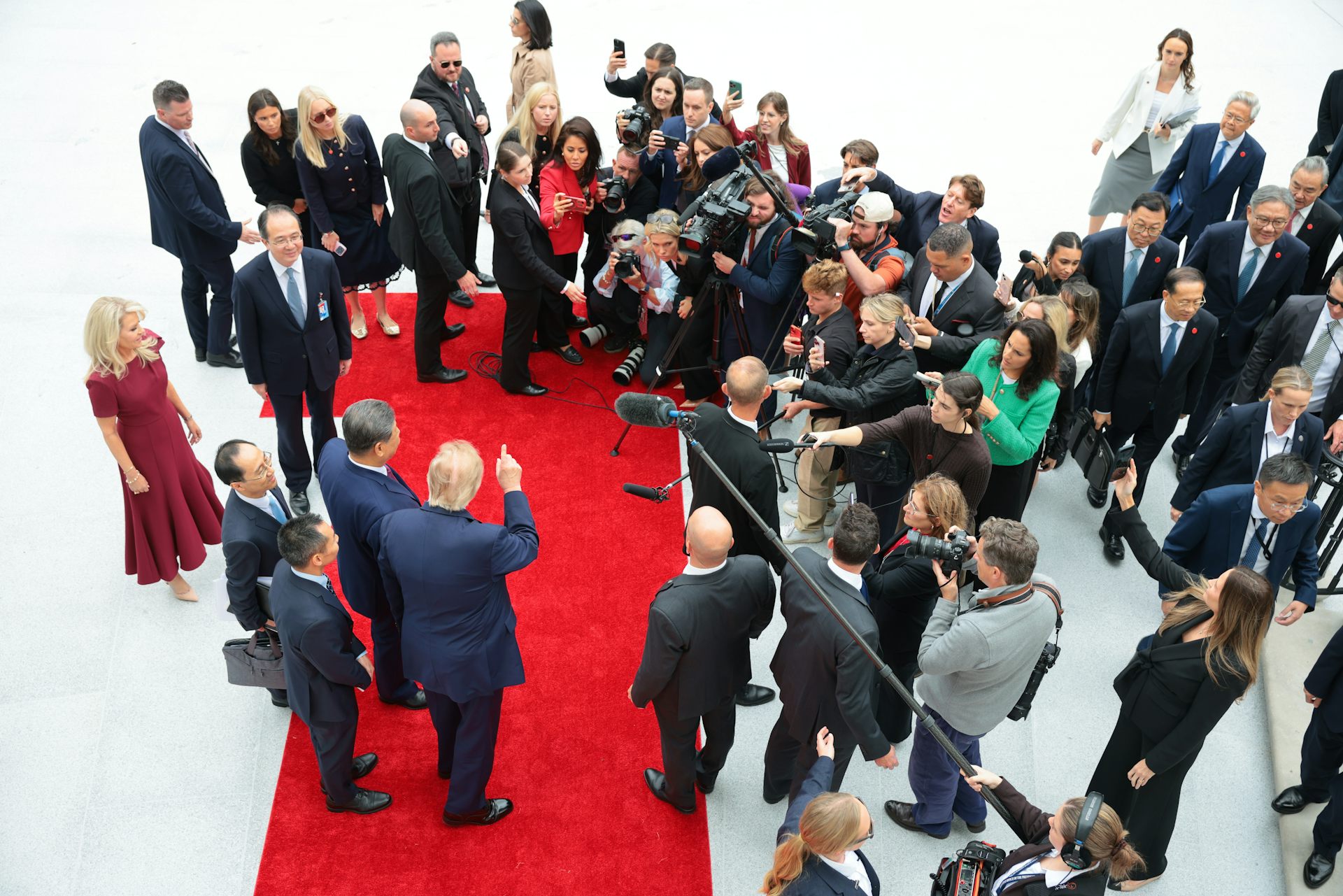 Four men on a red carpet speak to dozens of people holding cameras and microphones.