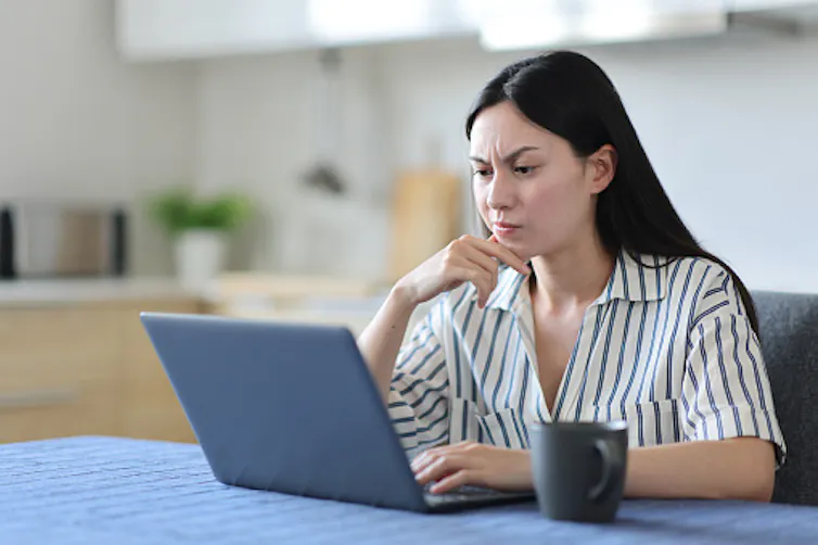 A woman frowns at her laptop screen.