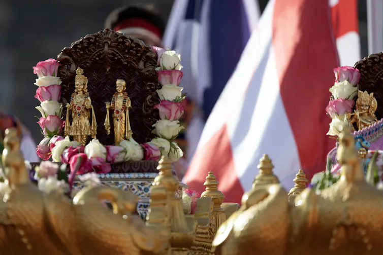 Hindu religious statues adorned with pink and white roses, displayed on decorated platforms with flags next to them.