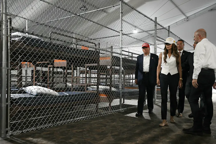five people look at bunk beds behind fencing