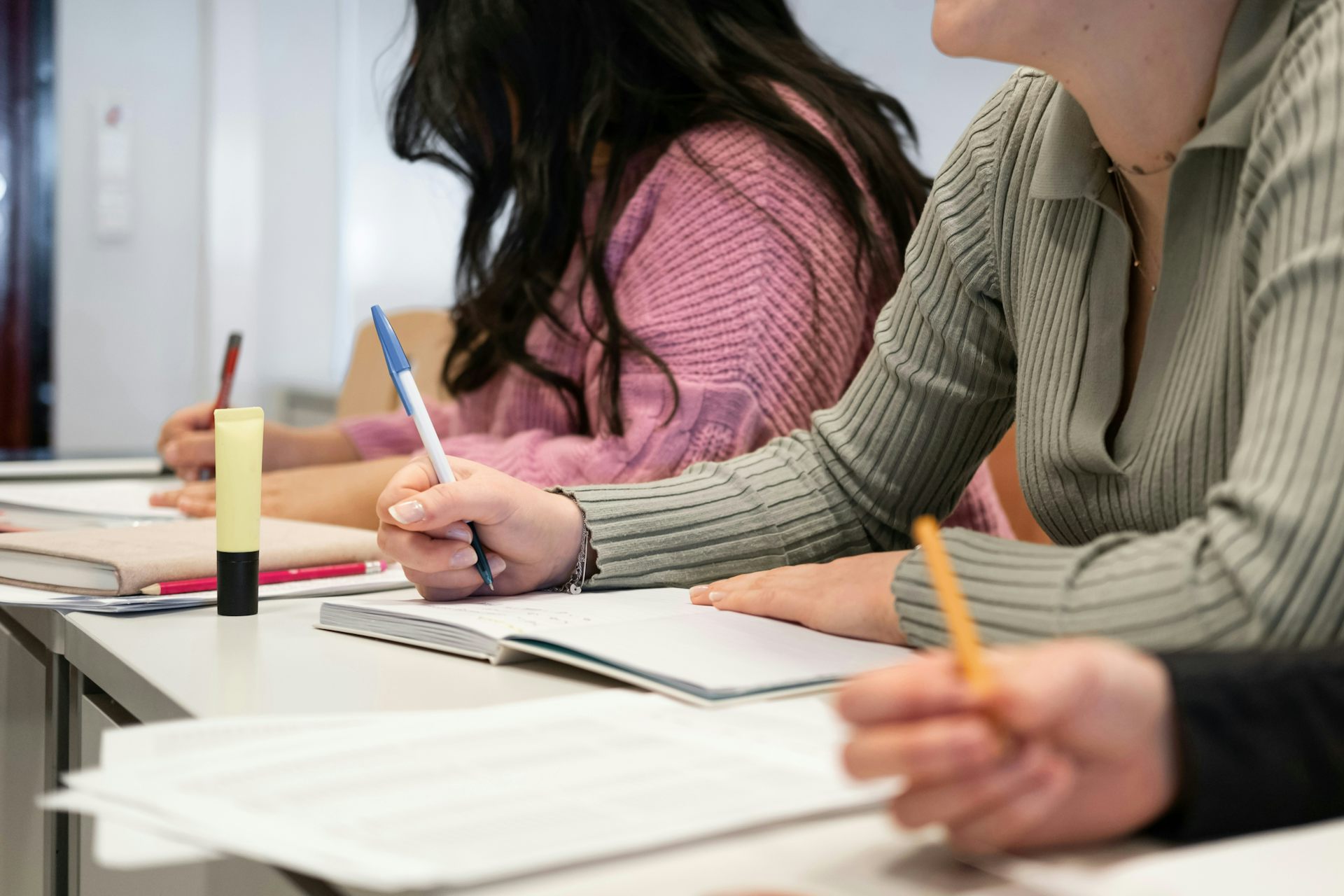 Students' hands holding pencils and pens at desks writing an assigment. 