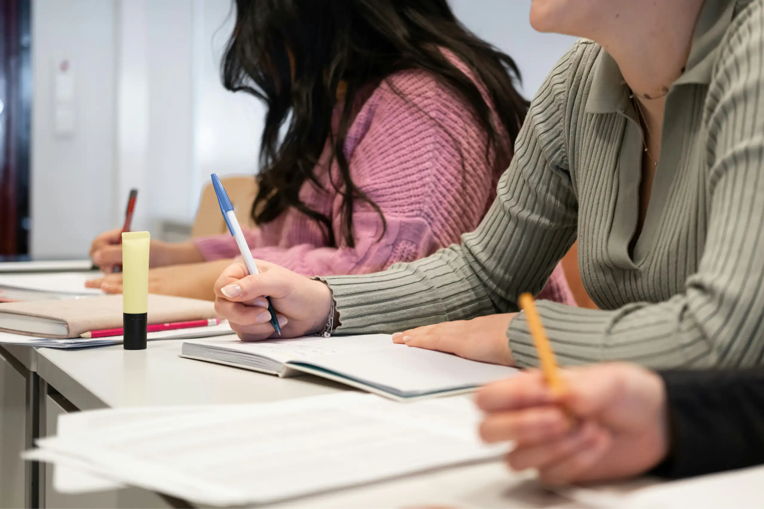 Students' hands holding pencils and pens at desks writing an assigment.