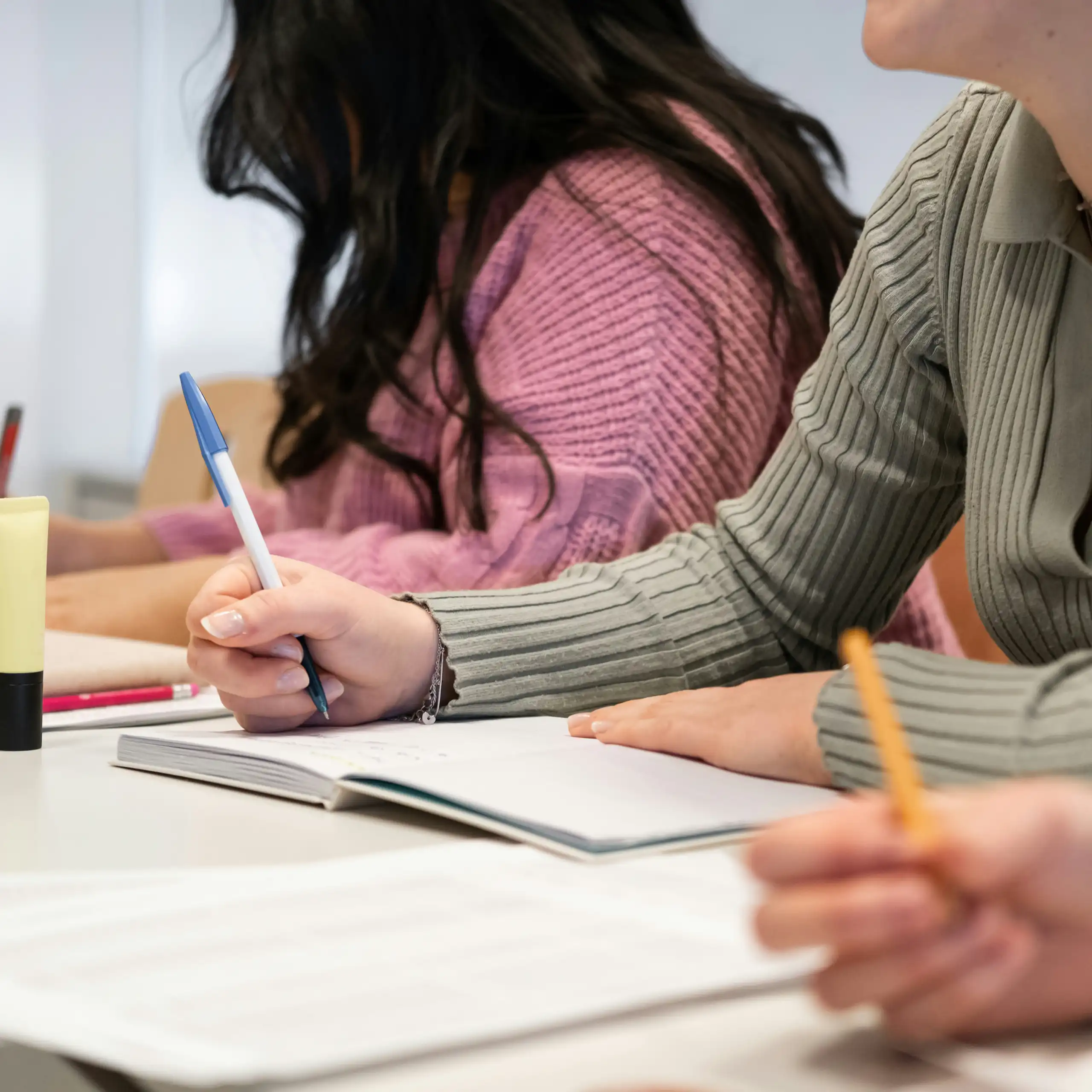 Students' hands holding pencils and pens at desks writing an assigment.
