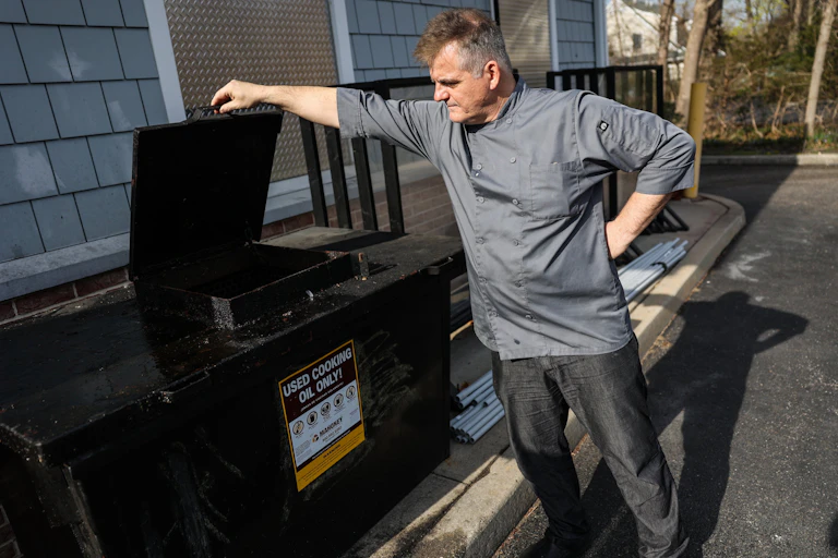 A man stands next to a large black container labeled 'Used cooking oil only.'