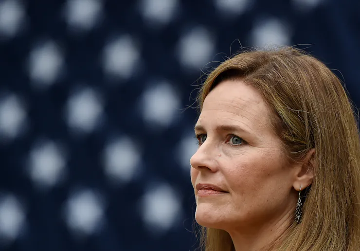 A woman with brown hair looking pensive, with an American flag behind her.
