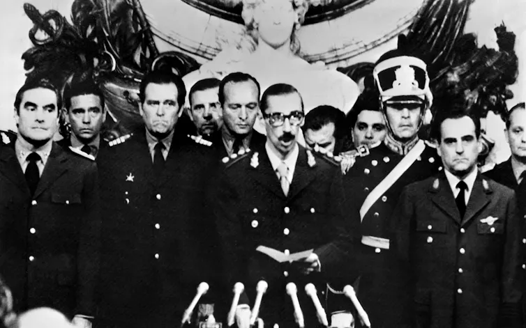 A black and white image shows a group of men in military uniform at an official event.