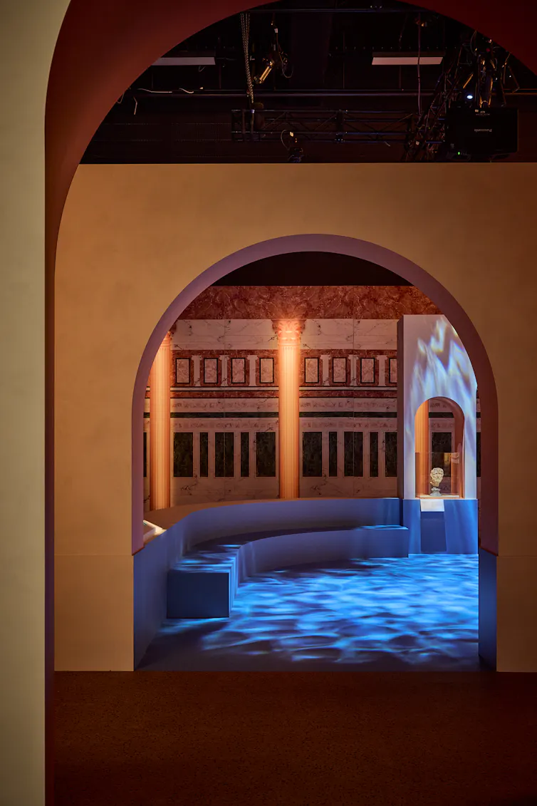 Darkened gallery space showing a reproduction of a bathhouse, through an archway.