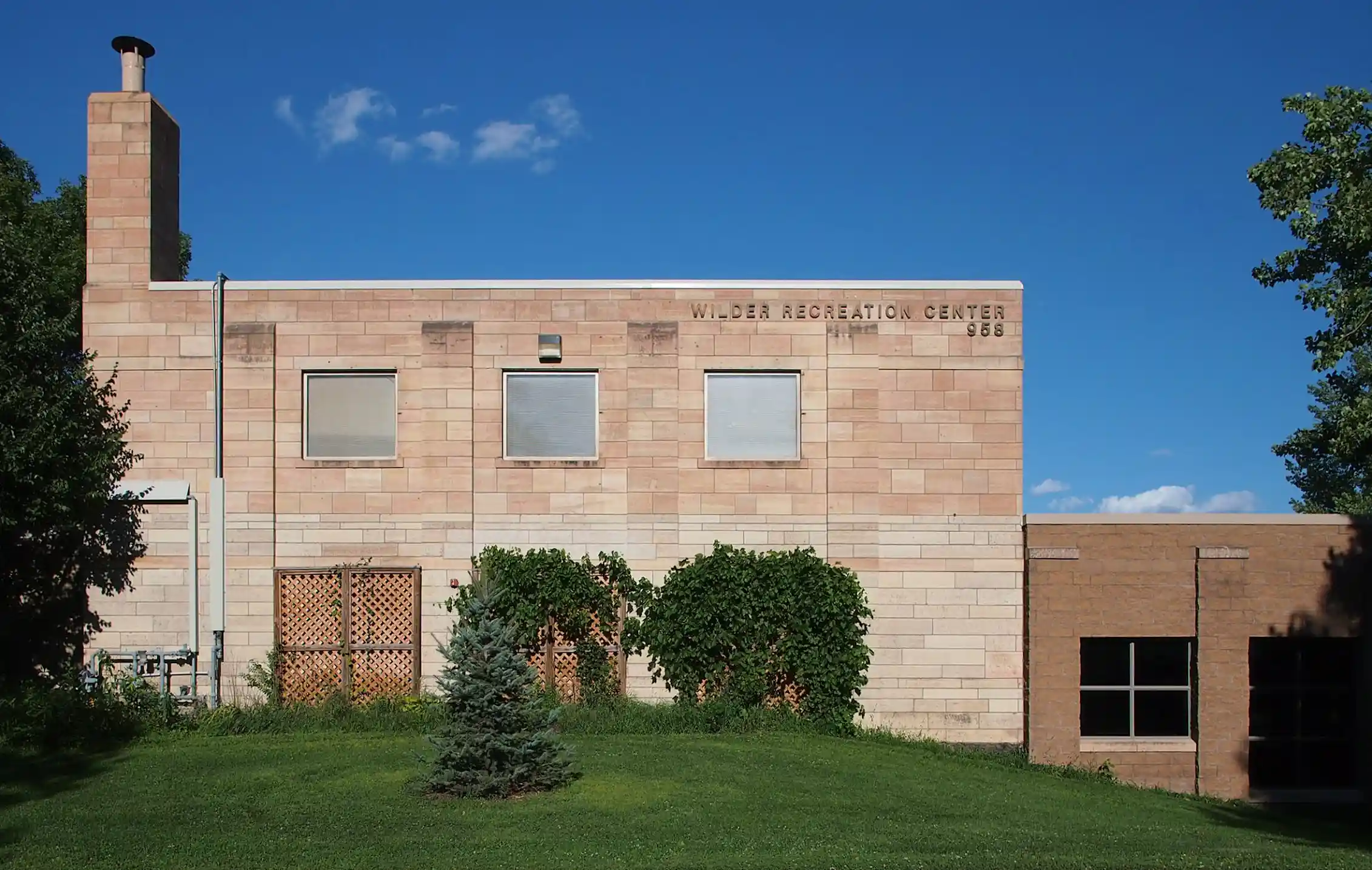 A tan stone building sits on a plot of land with a green yard and a few trees.