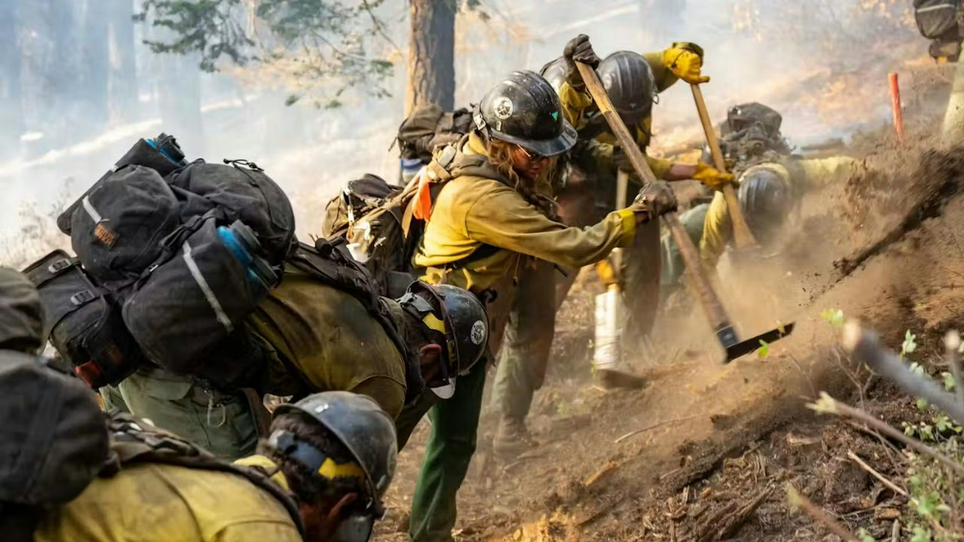 A group of firefighters climing a dusty hill. The hill is steep and the firefighters appear tired.