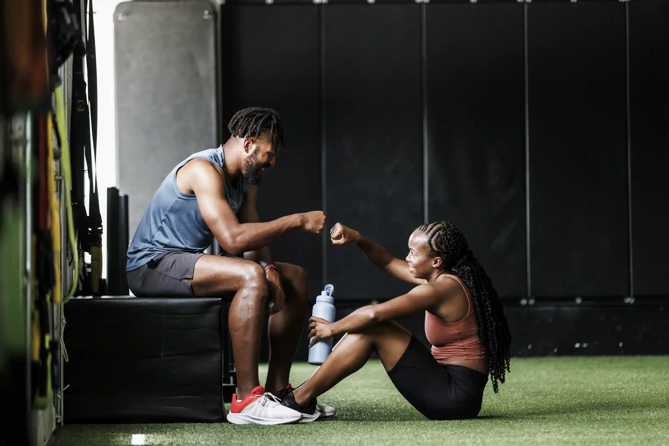 Two people sitting inside a gym, fit bumping