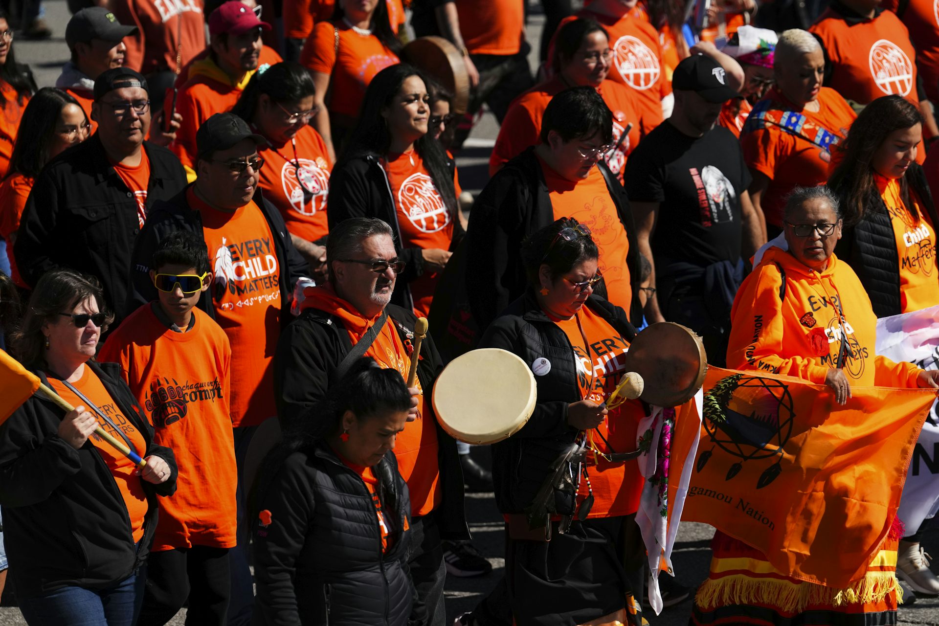 A group of people wearing orange stand on the street. A drum is visible in the centre.
