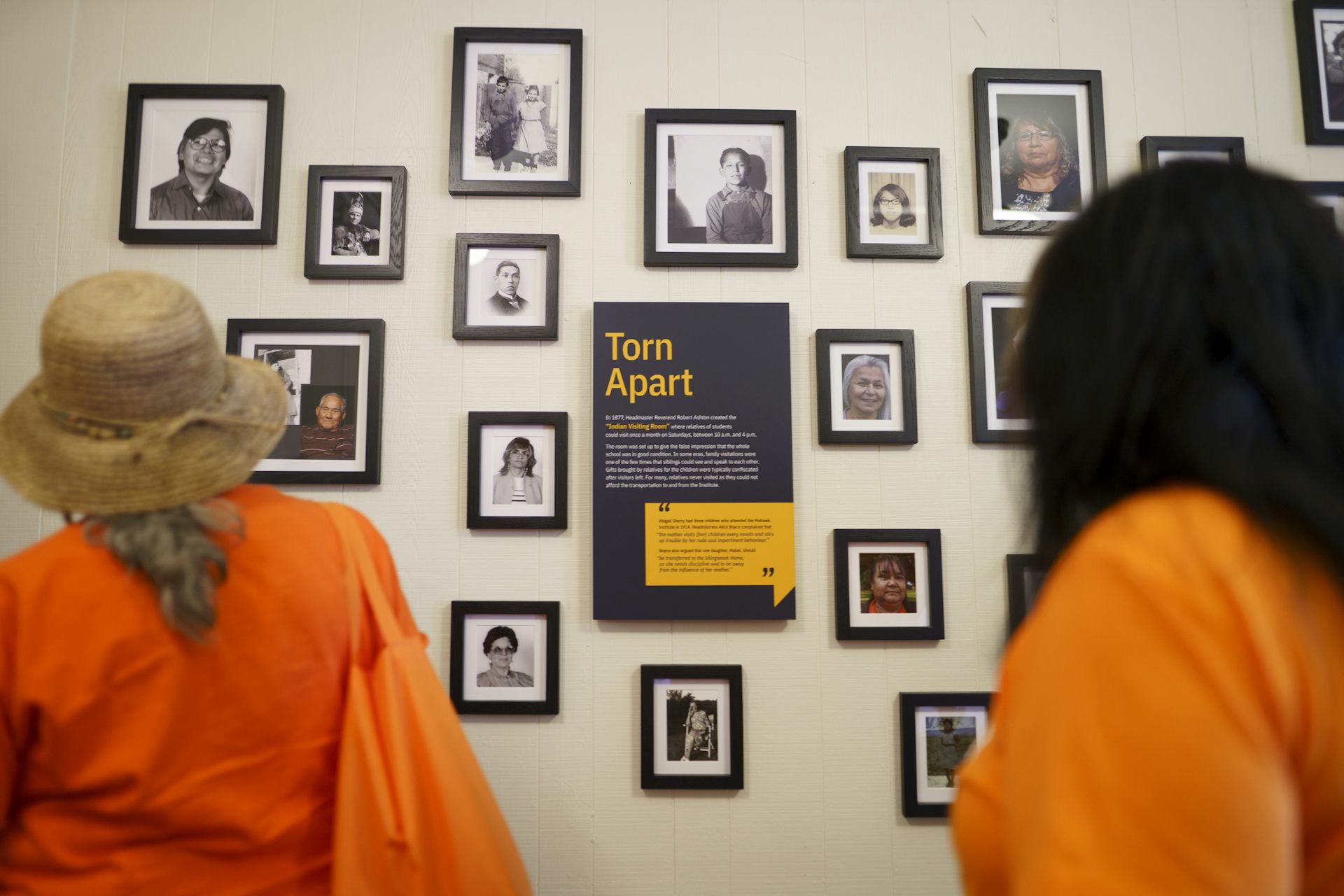 two people wearing orange look at wall that has several framed black and white photos on it