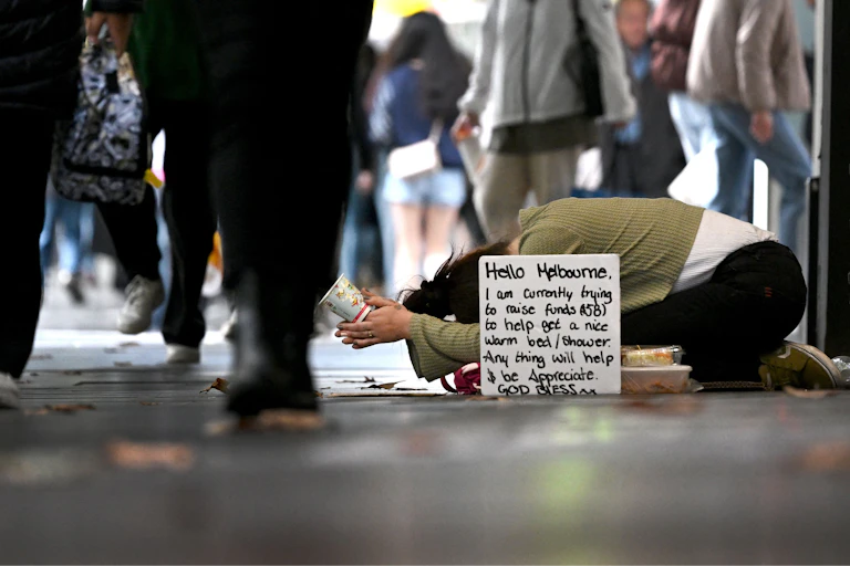 A homeless person is seen as people walk by on a busy street.