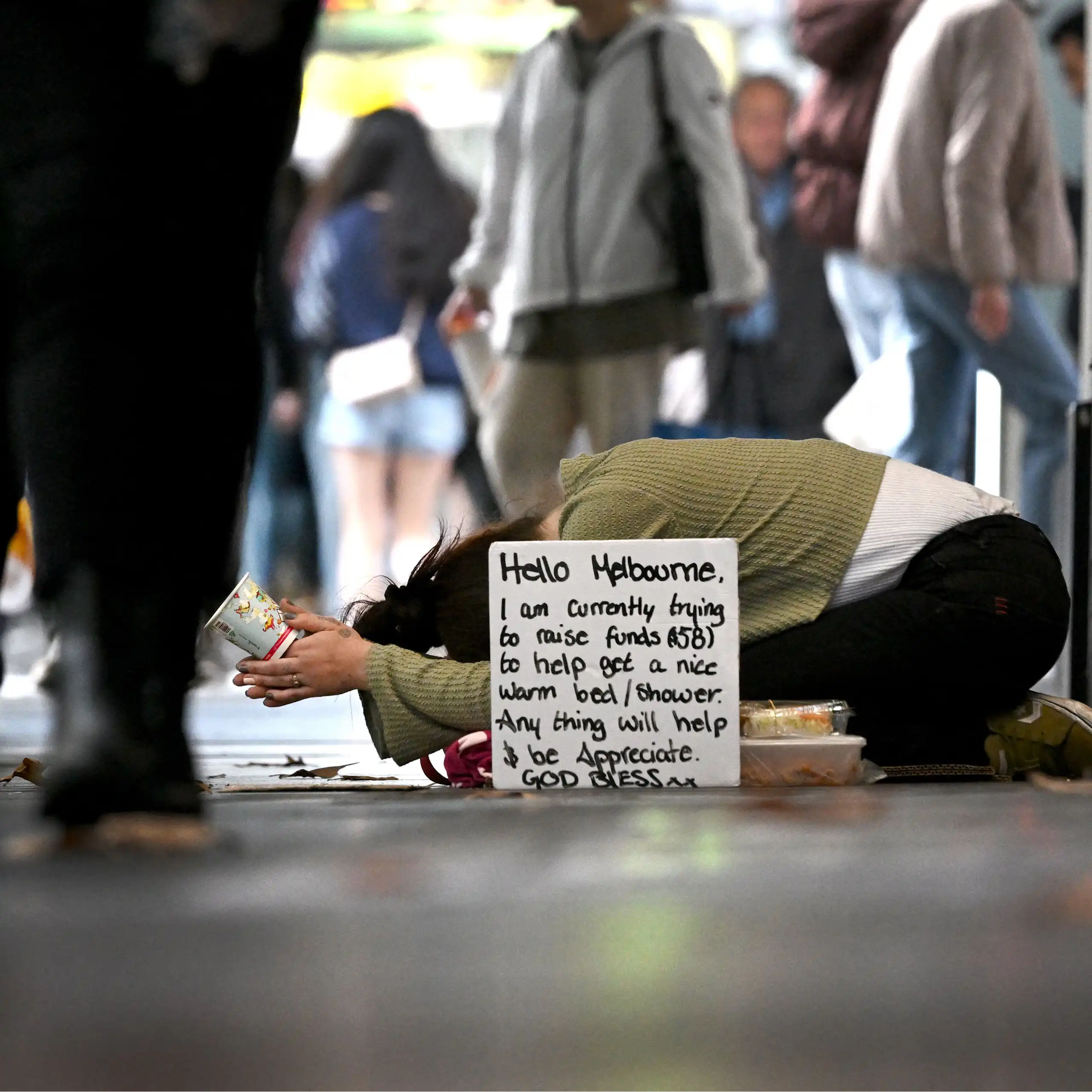 A homeless person is seen as people walk by on a busy street.