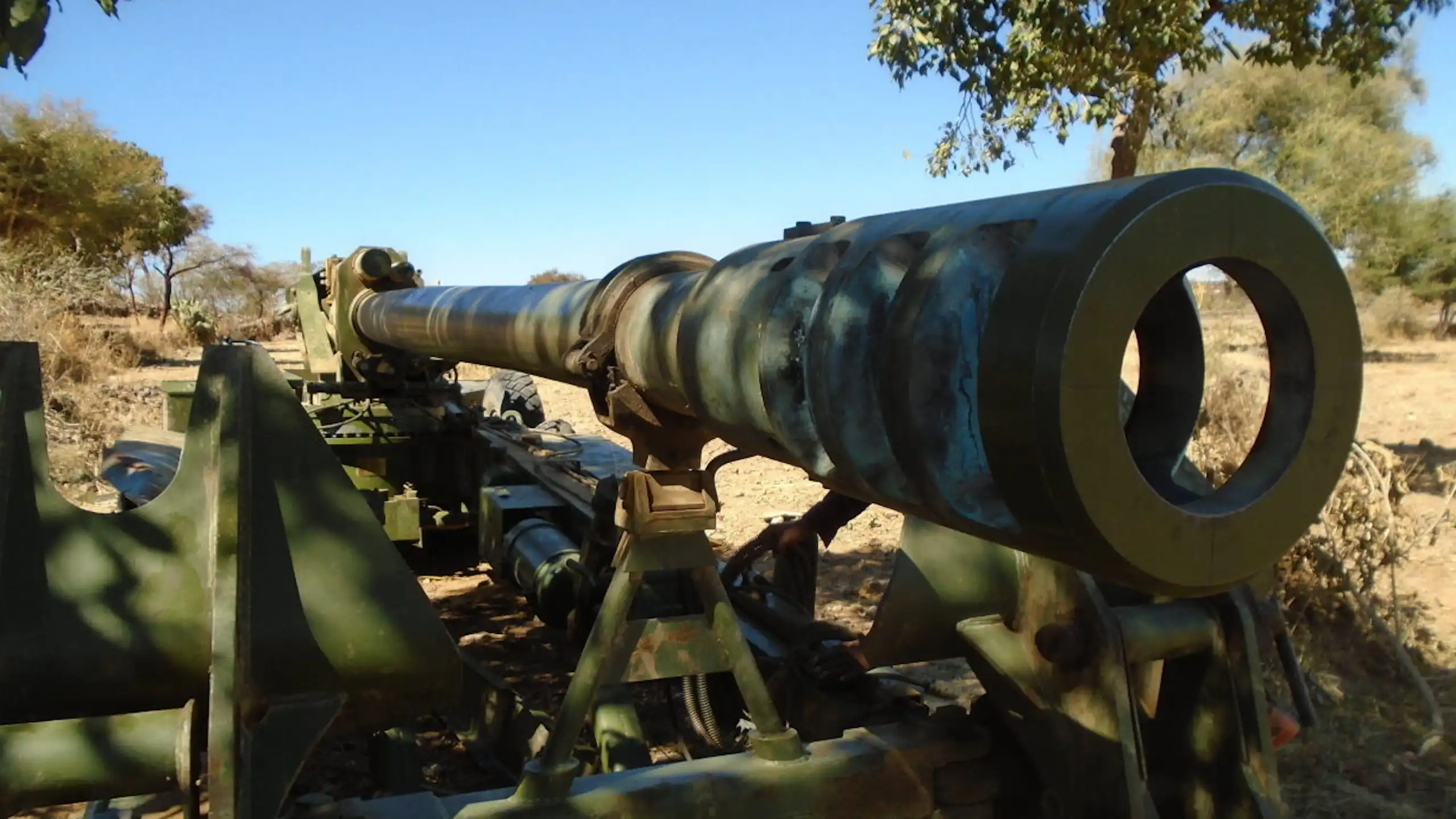 A large green metal piece of equipment with a scope that's lying on arid ground
