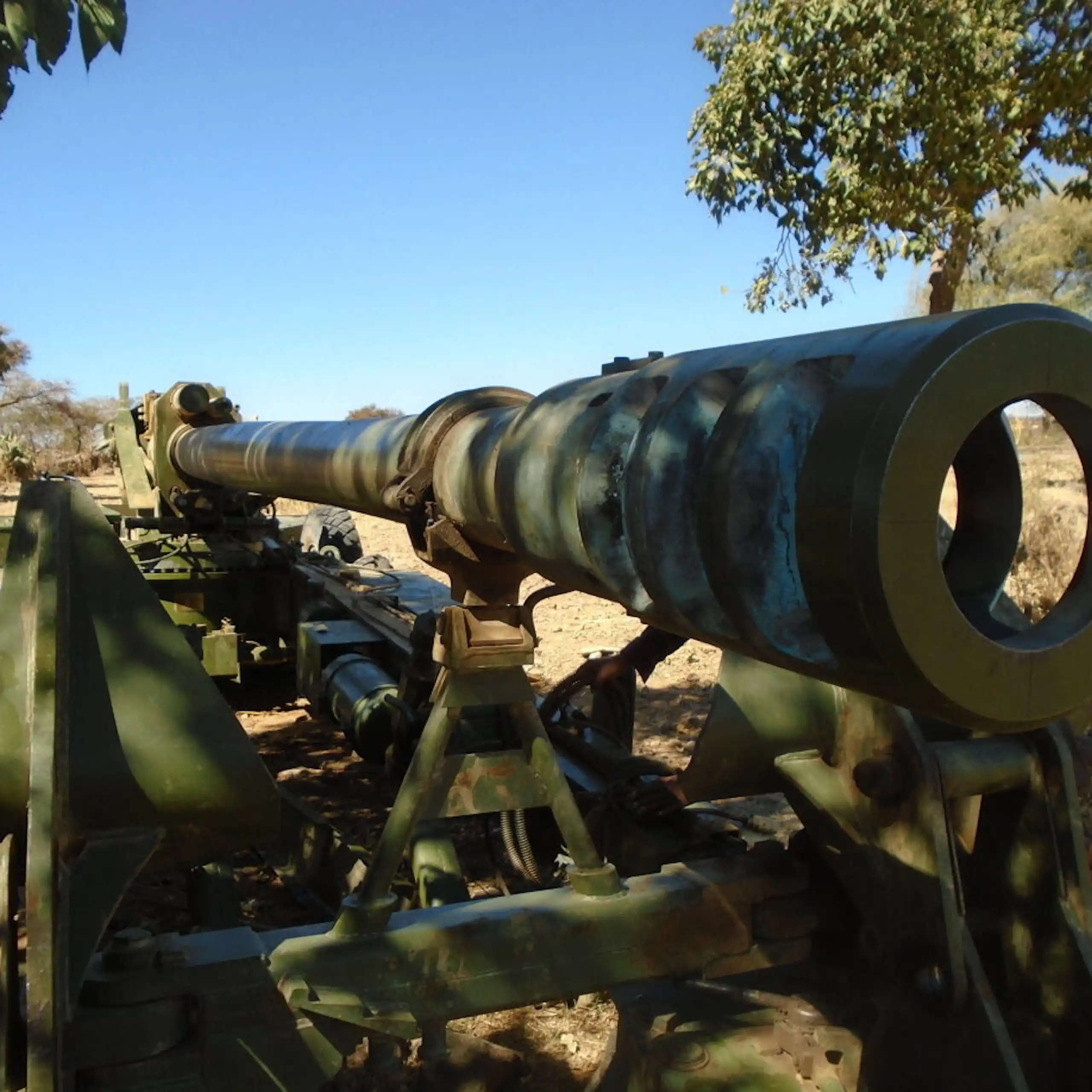 A large green metal piece of equipment with a scope that's lying on arid ground