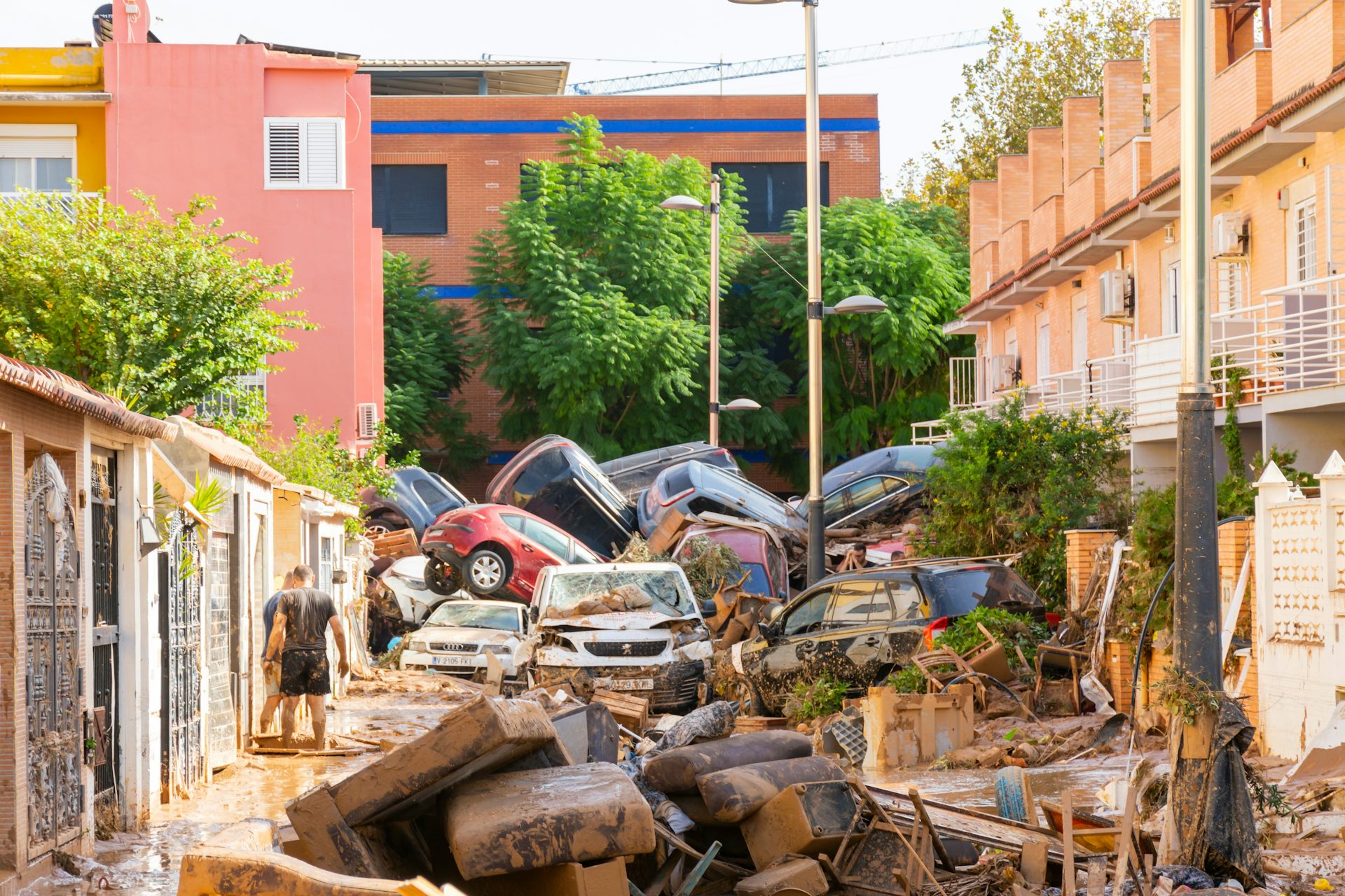 Dos persones en un carrer després de les inundacions, amb mobles, cadires i una muntanya de cotxes enmig dels edificis.