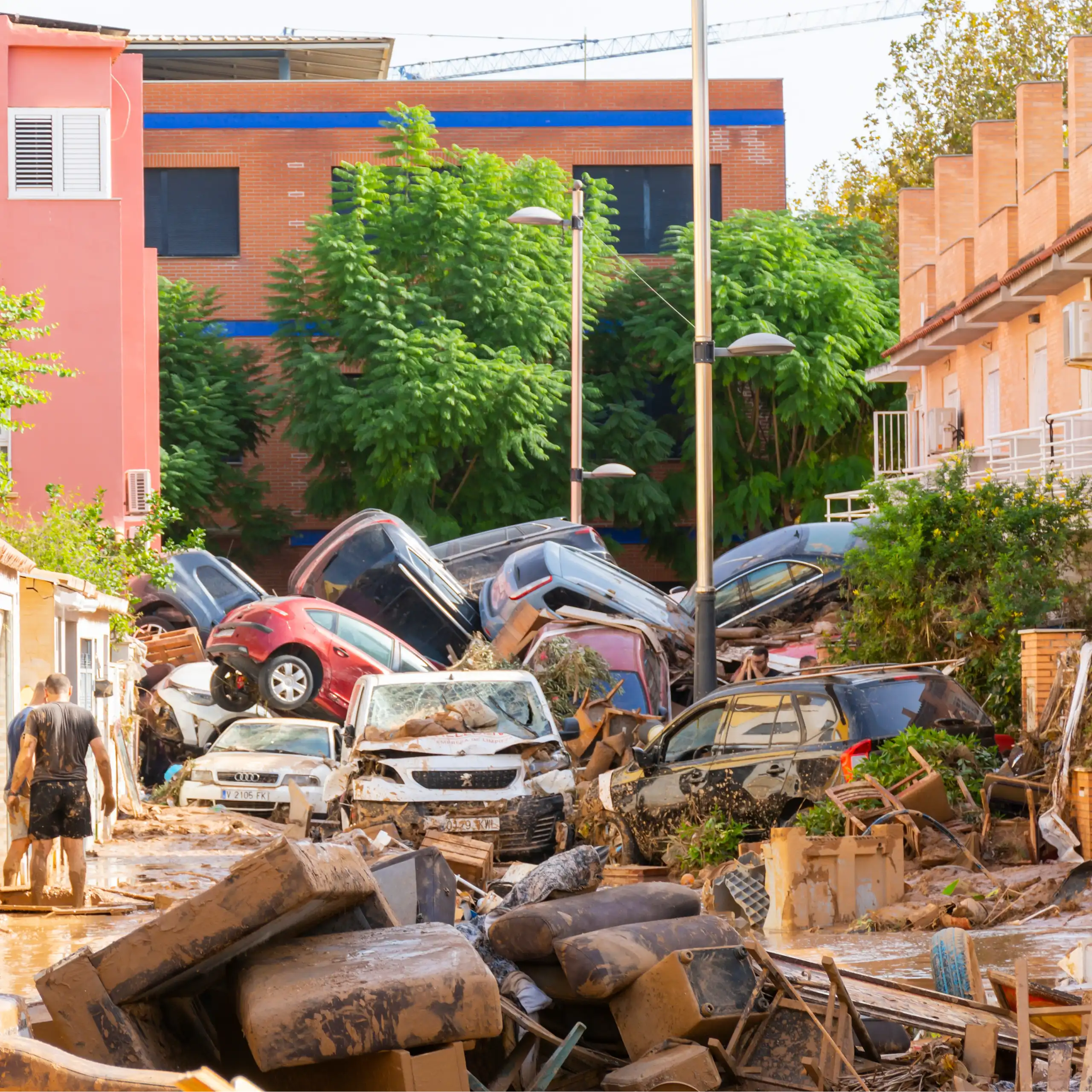 Dos persones en un carrer després de les inundacions, amb mobles, cadires i una muntanya de cotxes enmig dels edificis.